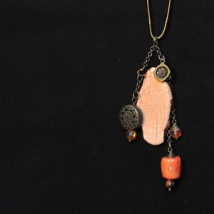 May include: A gold chain necklace with a pendant featuring a peach-colored stone, a small gold charm, and coral-colored beads.