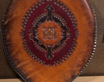 May include: A brown leather oval-shaped pouch with a zipper closure and intricate tooled design in shades of brown, red, and gold.