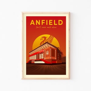 May include: A framed art print featuring Anfield stadium in a stylized illustration. The artwork is dominated by shades of red and orange, with the word "ANFIELD" in yellow at the top. The phrase "You'll never walk alone" is below the word "ANFIELD".
