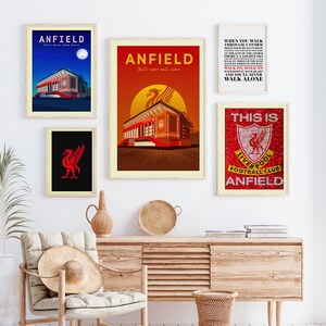May include: A collection of framed art prints featuring the word "ANFIELD" and the Liverpool Football Club logo. One print shows the stadium at night, another at sunset, and a third with the text "You'll Never Walk Alone."