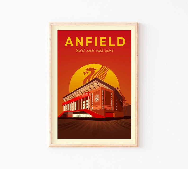 May include: A framed art print featuring Anfield stadium in a stylized illustration. The artwork is dominated by shades of red and orange, with the word "ANFIELD" in yellow at the top. The phrase "You'll never walk alone" is below the word "ANFIELD".