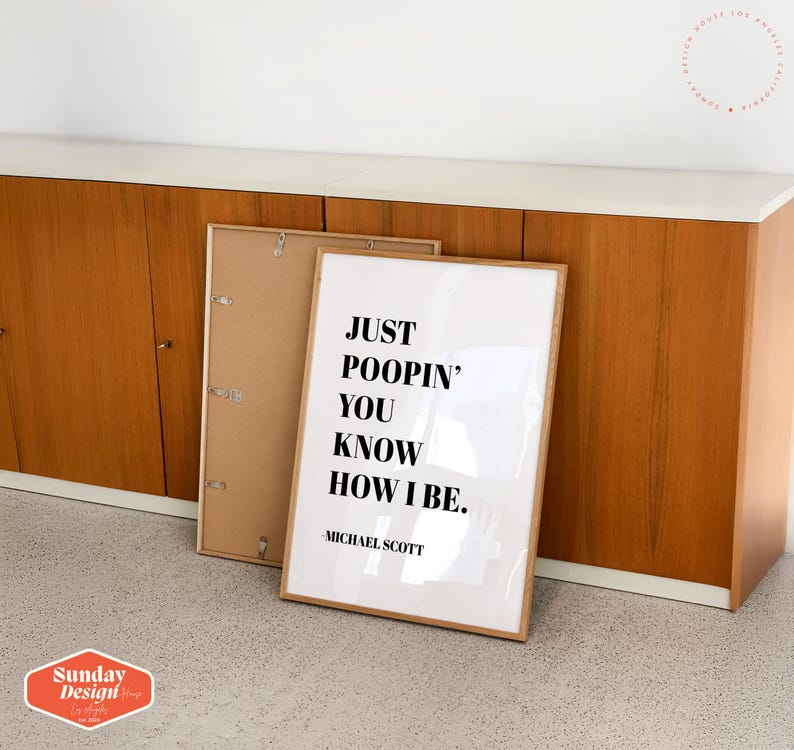 Op de afbeelding: Een witte ingelijste print met de tekst "Just poopin' you know how I be." en "Michael Scott" onderaan. De print leunt tegen een houten kast.
