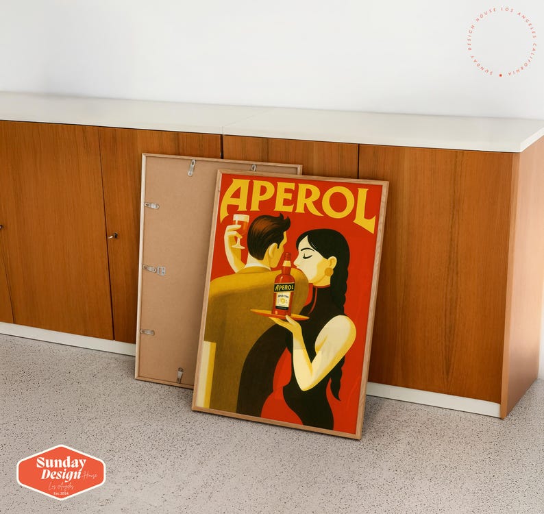 May include: A vintage poster advertising Aperol, featuring a couple in a romantic setting. The poster has a red background with the word "Aperol" in white letters. The couple is dressed in stylish clothing and is holding a bottle of Aperol.
