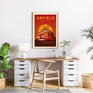 May include: Framed art print featuring a stylized illustration of Anfield stadium. The artwork displays the stadium in shades of red and brown against a sunset backdrop, with the text "ANFIELD" and "You'll never walk alone".