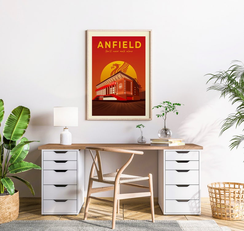 May include: Framed art print featuring a stylized illustration of Anfield stadium. The artwork displays the stadium in shades of red and brown against a sunset backdrop, with the text "ANFIELD" and "You'll never walk alone".