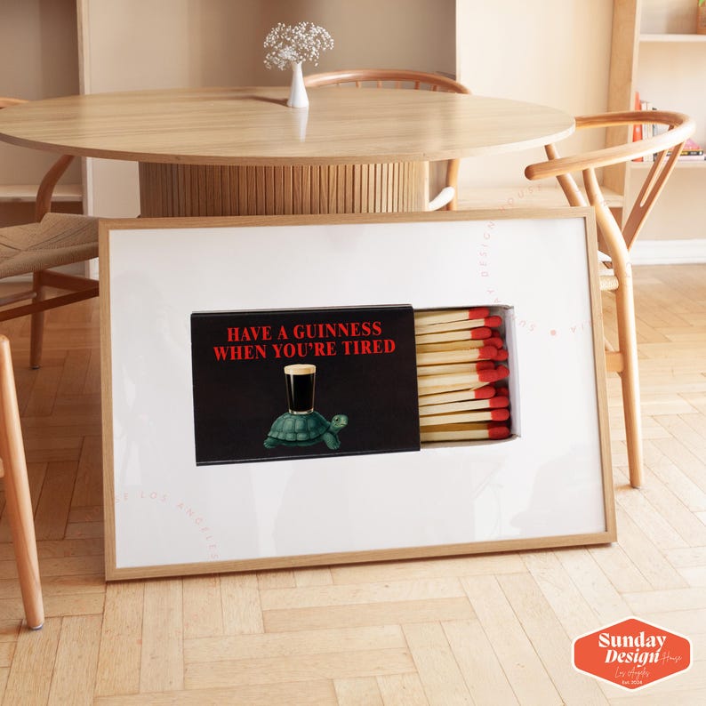 May include: A framed art print featuring a matchbox design with the text "HAVE A GUINNESS WHEN YOU'RE TIRED." The artwork includes a Guinness glass on a turtle. The matchsticks have red tips. The frame is light wood.