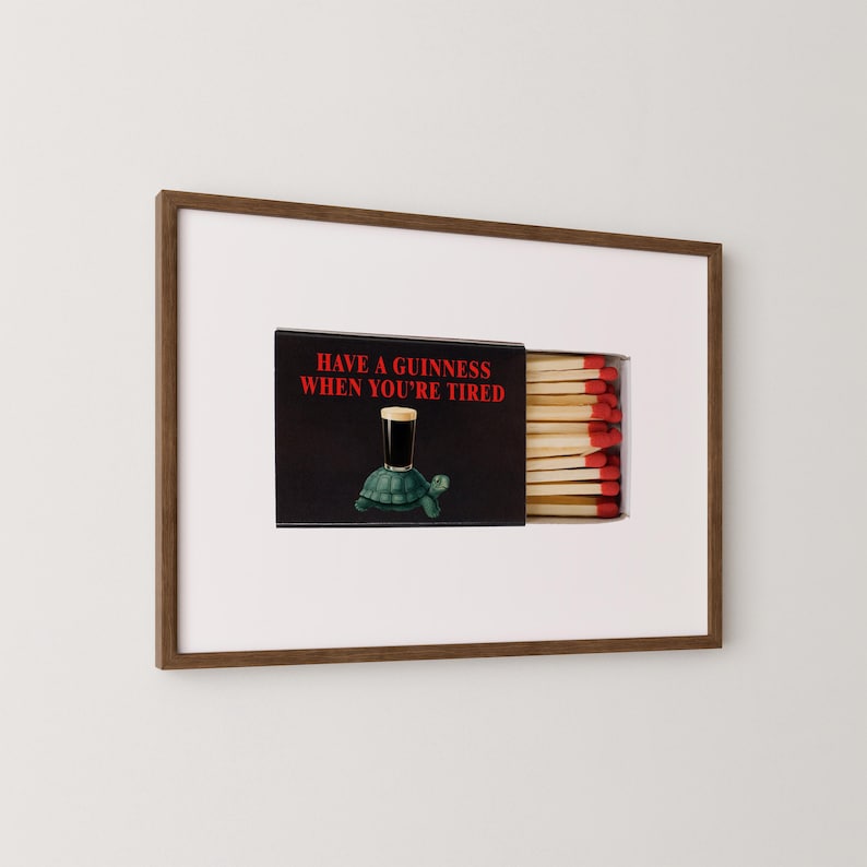 May include: A framed artwork featuring a matchbox with the text "HAVE A GUINNESS WHEN YOU'RE TIRED" and a cartoon turtle holding a pint of Guinness. The matchbox is open, revealing the matchsticks.