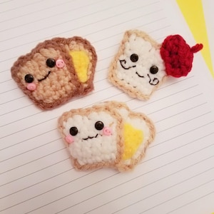 May include: Three crocheted toast plush toys. One is brown with a yellow center, one is white with a yellow center, and one is white with a red crocheted beret.