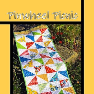 May include: A colorful quilt with a pinwheel design, featuring red, yellow, blue, green, and white fabric. The quilt is laid out on a rock in a grassy area. The text "Pinwheel Picnic" is at the top of the image, and the text "Tricia Lynn Maloney Orphan Quilt Designs For Villa Rosa Designs" is at the bottom.