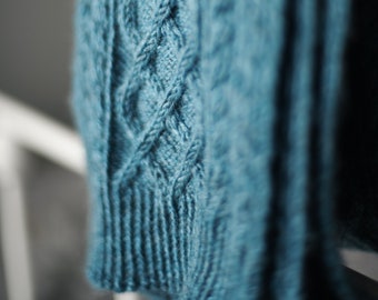May include: A close-up of a teal blue knitted sweater with a cable knit pattern.