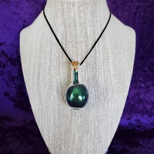 May include: A green glitter filled glass bottle pendant on a black cord necklace. The bottle has a cork stopper.