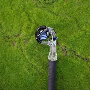 May include: A glass pipe with a black and white striped sphere on top. The pipe is clear glass and has a black rubber grip.