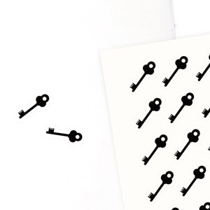 May include: A sheet of black key stickers with the text "Olivia Planner Factory" at the bottom. Two keys are shown on a white notebook page.
