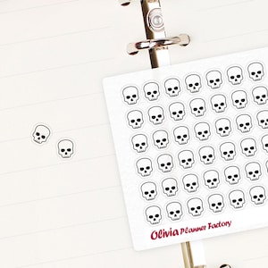 Peut inclure: Une feuille d'autocollants blancs avec 49 autocollants de crânes noirs et blancs. La feuille d'autocollants est étiquetée "Olivia Planner Factory" et "L455".