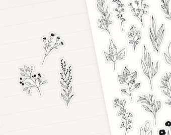 May include: A sheet of white sticker paper with black line drawings of various flowers and plants. The stickers are arranged in rows and columns on the sheet. The sheet is on a pink surface.
