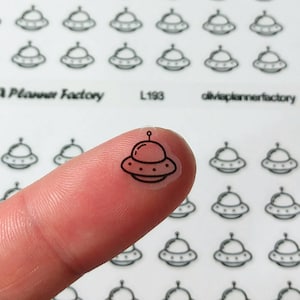 Peut inclure: Une feuille d'autocollants transparents avec des dessins de soucoupes volantes en noir. Les autocollants sont petits et parfaits pour les planificateurs ou les journaux. La feuille porte l'inscription "Olivia Planner Factory" et "L193".