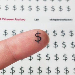 Puede incluir: Una hoja de pegatinas transparentes con un signo de dólar negro impreso en cada pegatina. Las pegatinas son pequeñas y se muestran en un dedo.