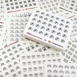 May include: A collection of white planner stickers with various black line art designs. The stickers feature images of envelopes, gifts, laundry machines, and other icons. The brand name "Olivia Planner Factory" is visible.
