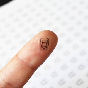 May include: A small, clear sticker with a black outline of a person wearing a swimsuit.