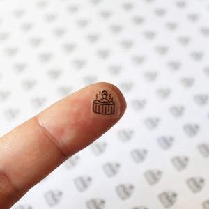 May include: A small black and white sticker of a person in a hot tub with steam rising from the water.