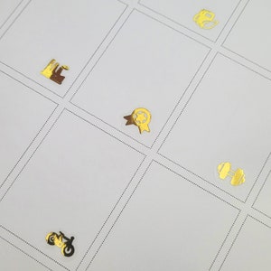 May include: A white grid with various gold foil stickers. The stickers include a factory, a star-shaped award ribbon, a motorcycle, a dumbbell, and a tea kettle. The grid is divided by dotted lines.