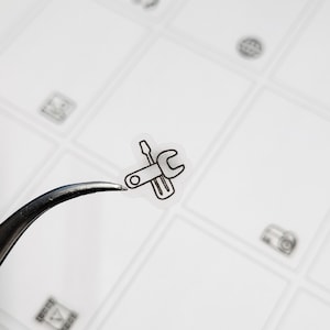 May include: A clear sticker with a black outline of a wrench and screwdriver, representing tools.