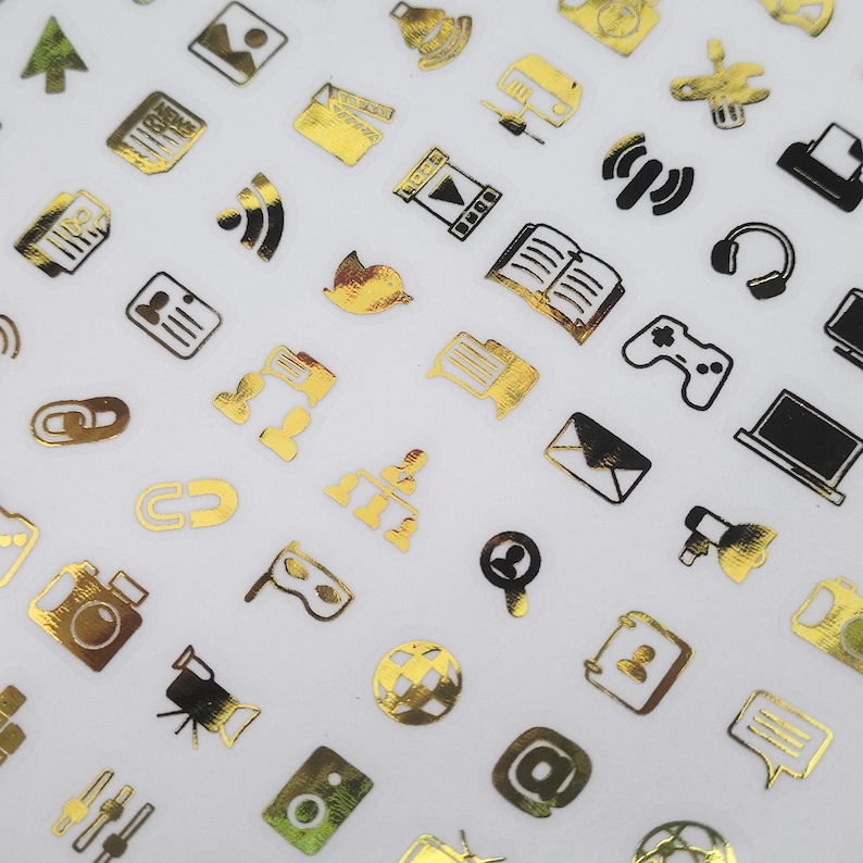 May include: A selection of gold and black icon stickers, including a camera, headphones, a laptop, and a video camera. The stickers are arranged on a white background. The icons represent various communication and media symbols.