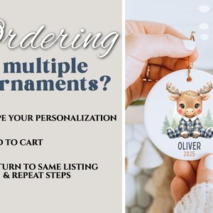 May include: A round Christmas ornament featuring a cartoon moose in a plaid outfit, with the name "OLIVER" and the year "2025" printed on it. The ornament is held by a person. The text "Ordering multiple ornaments?" is also visible.