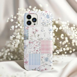 May include: A white phone case with a patchwork design featuring floral and geometric patterns in shades of pink, blue, and white.