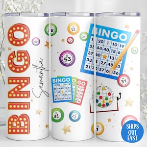 May include: White tumbler featuring a bingo theme. The design includes the word "BINGO" in marquee-style lettering, bingo cards, and bingo balls. The name "Samantha" is also displayed. A blue circle with the text "SHIPS OUT FAST" is also visible.