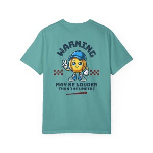 May include: A teal blue t-shirt with a cartoon baseball graphic and the text "WARNING MAY BE LOUDER THAN THE UMPIRE".
