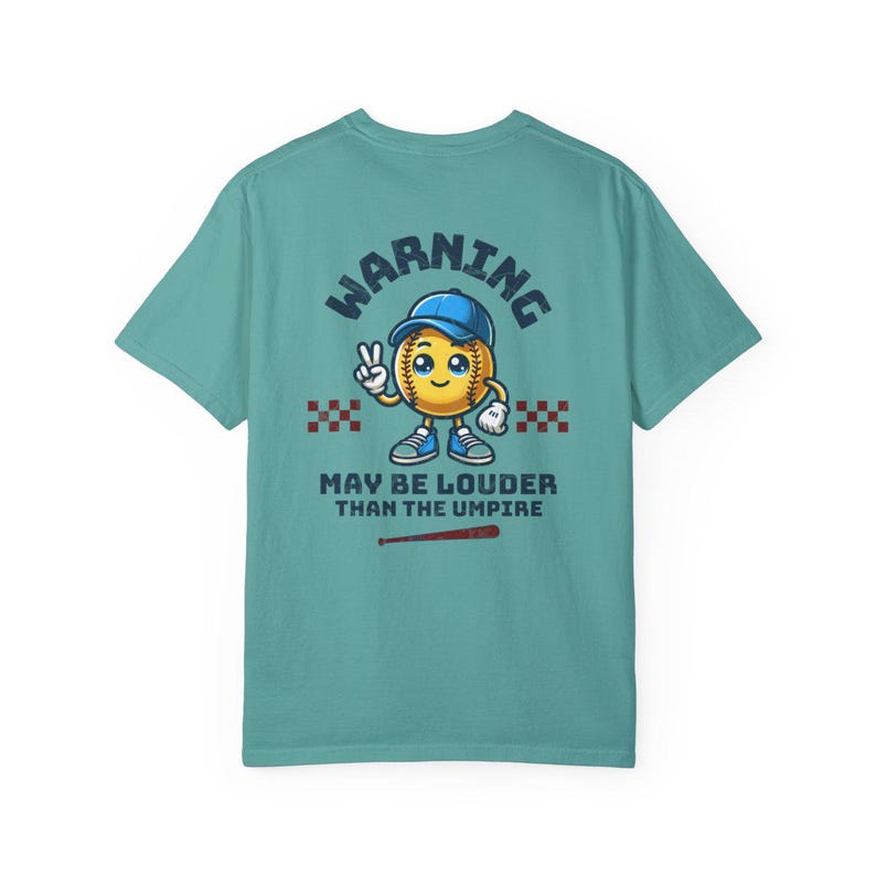 May include: A teal blue t-shirt with a cartoon baseball graphic and the text "WARNING MAY BE LOUDER THAN THE UMPIRE".