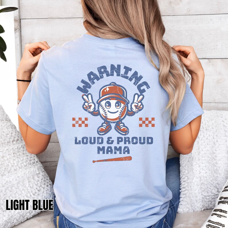 May include: Light blue t-shirt with a distressed graphic of a baseball with a face and the text "WARNING LOUD & PROUD MAMA" with a baseball bat underneath.