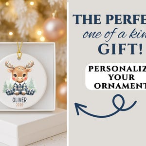 May include: A personalized Christmas ornament featuring a cartoon moose in a blue plaid outfit, sitting in front of pine trees. The ornament is white, with the name "Oliver" and the year "2025" printed on it. The text "The perfect one of a kind GIFT!" is also visible.