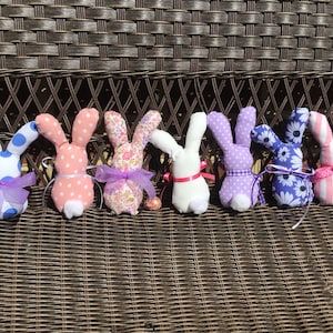 May include: Seven handmade fabric Easter bunny decorations. The bunnies are in various colors and patterns, including blue and white polka dots, pink and white polka dots, floral print, white, purple and white polka dots, blue and white floral print, and pink and white stripes.