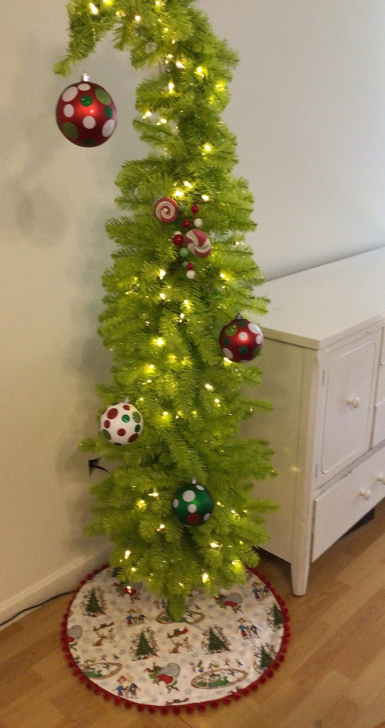 May include: A green artificial Christmas tree with white lights and red and green ornaments. The tree is decorated with candy canes and a red and white polka dot ornament. The tree is standing on a white and red tree skirt with a cartoon design.
