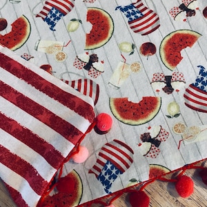 May include: A patriotic-themed fabric with a red and white striped border adorned with red and pink pom-poms. The fabric features a pattern of watermelon slices, lemonade, cupcakes, and American flag designs.