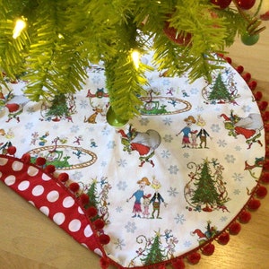 May include: A white Christmas tree skirt with a red and white polka dot trim and red pom-poms around the edge. The skirt features a whimsical illustration of characters from the book "The Grinch" by Dr. Seuss.