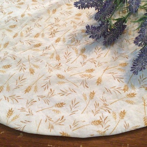 May include: A cream-colored fabric with a repeating pattern of wheat stalks in shades of gold and brown. The fabric is slightly curved, suggesting it is part of a larger piece. A sprig of purple lavender is in the upper right corner.