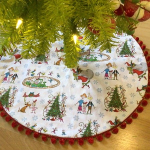 May include: A white Christmas tree skirt with a red pom-pom trim. The skirt features a whimsical illustration of characters from the classic children's book "How the Grinch Stole Christmas!"