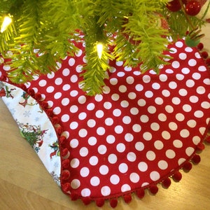 May include: Red and white polka dot Christmas tree skirt with a white pom-pom trim. The skirt is flipped over to show a white background with a Christmas tree and elves.