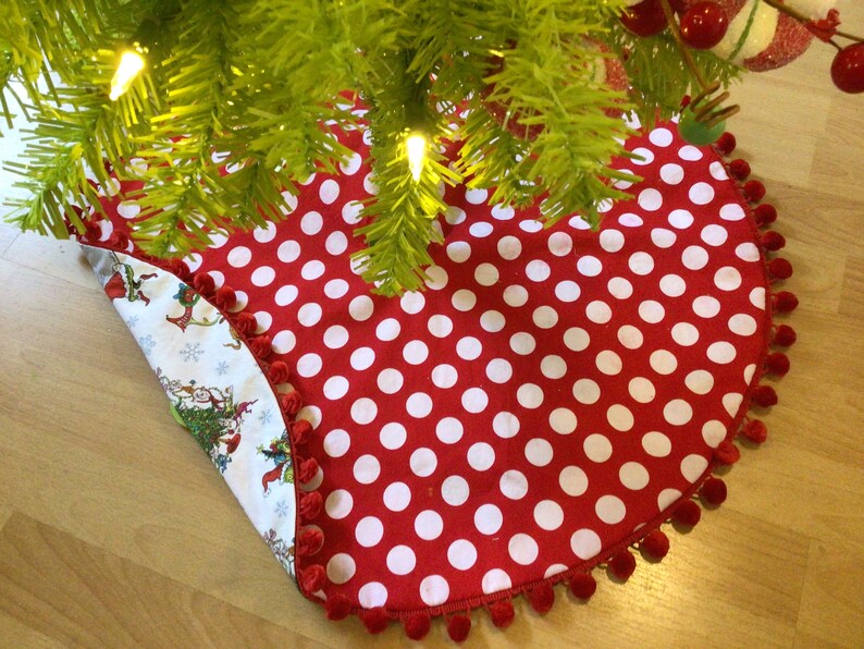 May include: Red and white polka dot Christmas tree skirt with a white pom-pom trim. The skirt is flipped over to show a white background with a Christmas tree and elves.