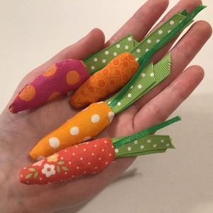 May include: Four handmade fabric carrots with green ribbon stems. The carrots are orange, pink, and red with white polka dots.