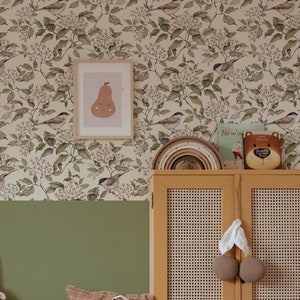 A vintage kid's room with a wooden dresser and birds beige and green wallpaper.