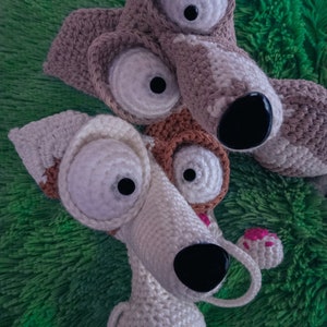 Puede incluir: Dos perros de peluche tejidos a crochet con ojos grandes. Un perro es marr&oacute;n y blanco, el otro es blanco con detalles marrones. Ambos perros tienen narices negras.