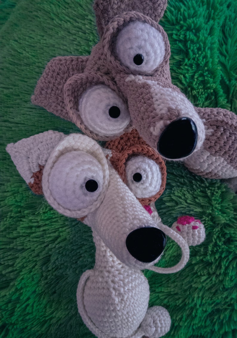 Puede incluir: Dos perros de peluche tejidos a crochet con ojos grandes. Un perro es marr&oacute;n y blanco, el otro es blanco con detalles marrones. Ambos perros tienen narices negras.