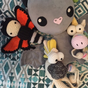 May include: A collection of crocheted stuffed animals, including a butterfly, a bat, a unicorn, and a bird. The animals are all made with different colored yarn and have unique features.