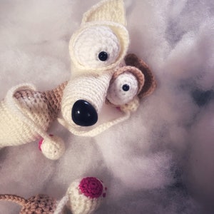 Puede incluir: Un juguete de perro de crochet blanco con detalles marrones y grandes ojos negros. El juguete tiene detalles rosas en las orejas y las patas.