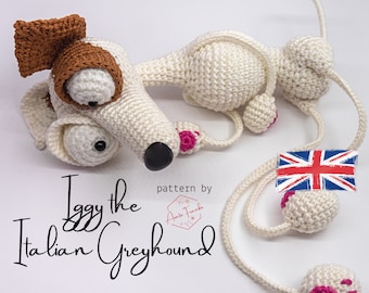 Puede incluir: Un perro italiano de pelo corto de crochet blanco llamado Iggy, con orejas marrones y almohadillas rosas. El perro está acostado de lado con la cabeza girada hacia un lado. El texto "Iggy the Italian Greyhound" está escrito debajo del perro. El texto "pattern by" está escrito encima del perro, con un pequeño logotipo debajo.