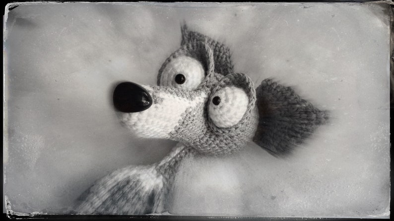 Puede incluir: Un animal de peluche de crochet blanco y negro con ojos grandes y un hocico largo. El animal est&aacute; acostado sobre una superficie blanca.